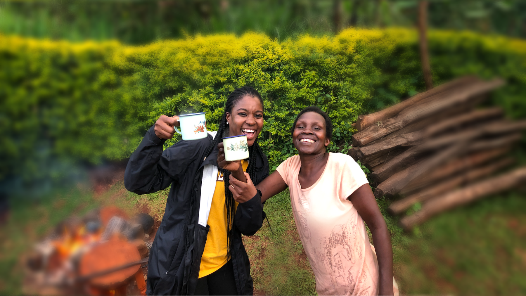 Bukky and a Ugandan woman hold up cups of hot coffee as if to cheers